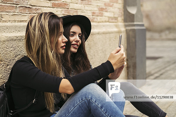 Two best friends sitting on the ground looking at smartphone