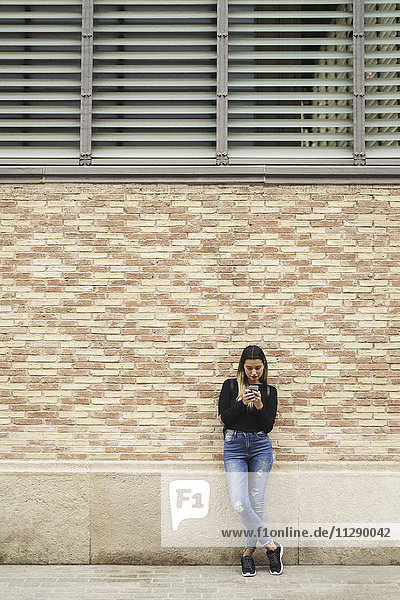 Junge Frau vor der Fassade mit Blick auf das Handy