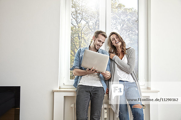 Happy couple standing in front of window with laptop