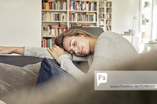 Junge Frau entspannt mit geschlossenen Augen auf der Couch im Wohnzimmer