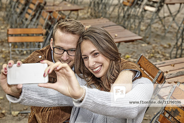 Glückliches Paar nimmt Selfie mit Smartphone im herbstlichen Biergarten mit