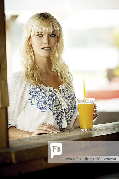 Porträt einer blonden Frau mit Getränk an der Strandhütte stehend