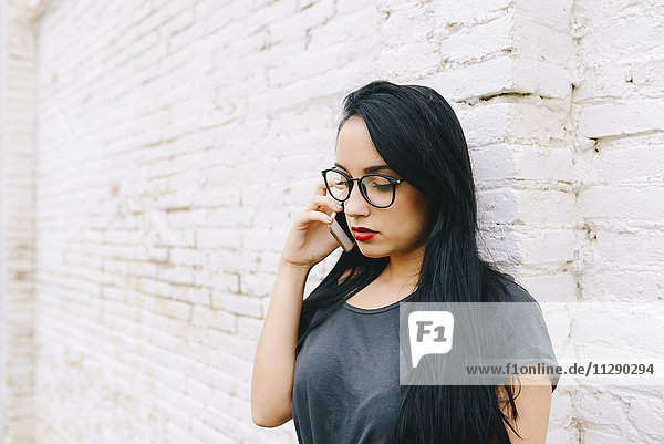 Young woman on cell phone in front of brick wall