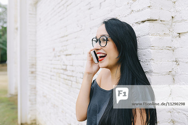 Happy young woman on cell phone in front of brick wall
