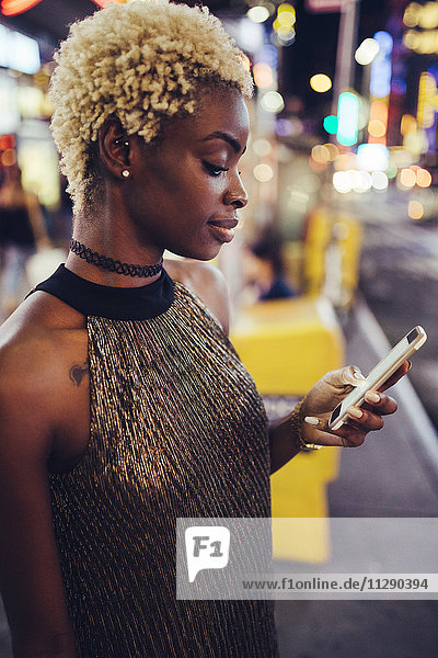 USA  New York City  junge Frau am Times Square bei Nacht mit Blick auf Smartphone