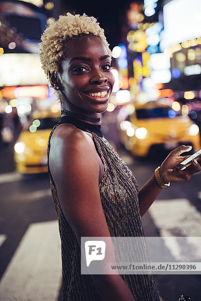 USA  New York City  Porträt einer lächelnden jungen Frau am Times Square bei Nacht