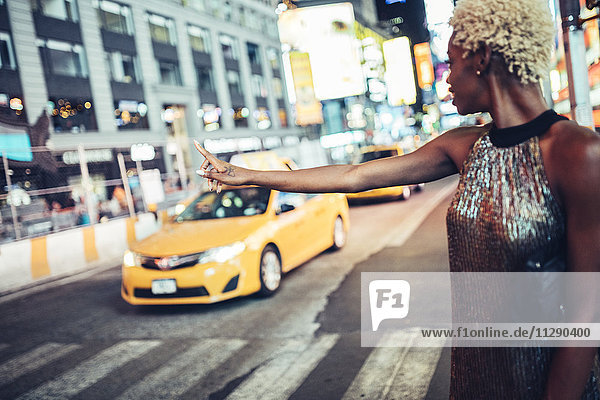 USA  New York City  junge Frau  die nachts am Times Square ein Taxi ruft.
