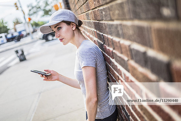 Woman with smartphone leaning against brick wall