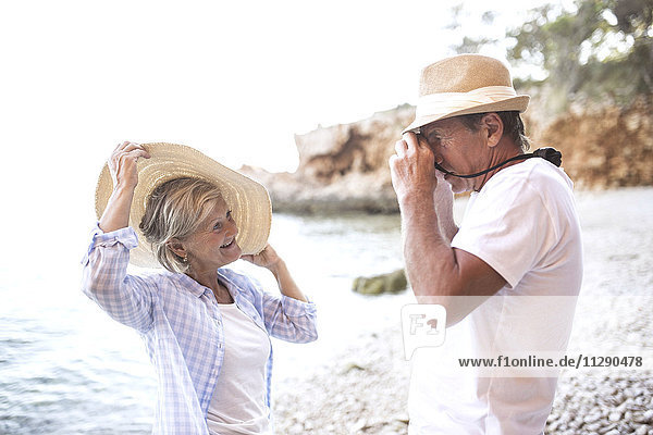 Älterer Mann beim Fotografieren seiner Frau am Strand