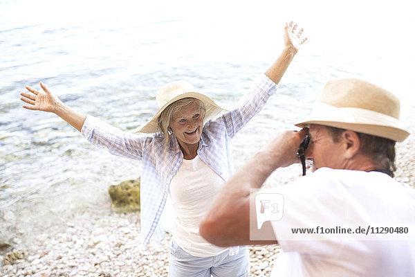 Älterer Mann beim Fotografieren seiner glücklichen Frau am Strand