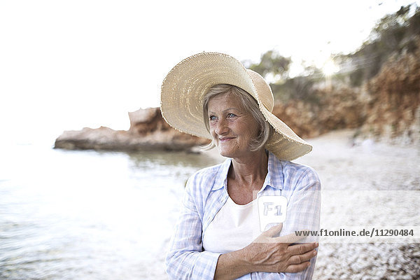 Porträt einer glücklichen reifen Frau mit Strohhut am Strand