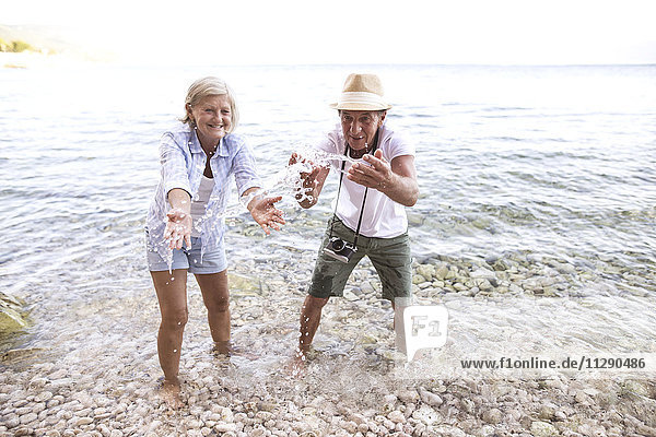 Senior couple splashing with water at seafront