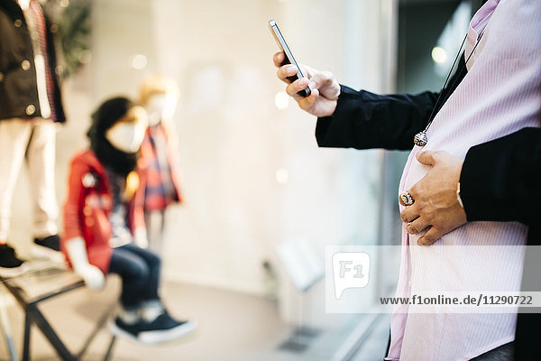 Schwangere mit Handy am Schaufenster