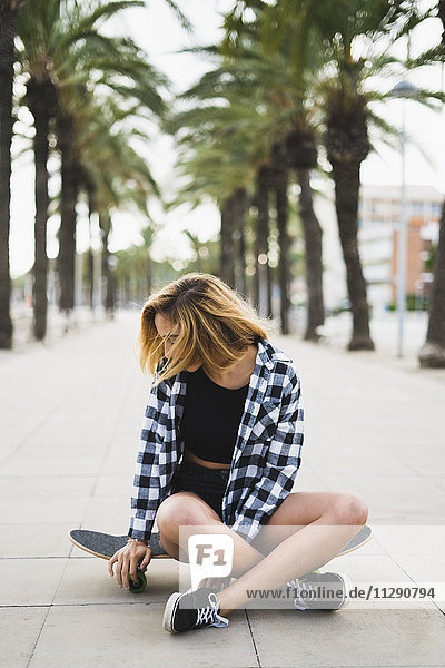 Spanien  junge Frau auf dem Skateboard sitzend