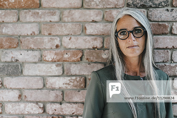 Portrait of woman with long grey hair in front of brick wall