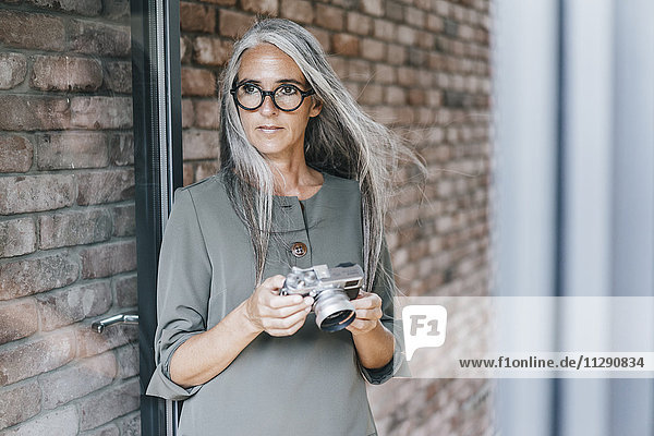 Frau mit langen grauen Haaren hält Kamera