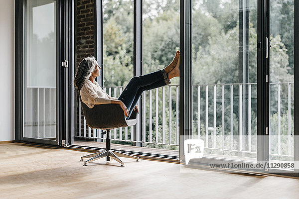 Frau mit langen grauen Haaren auf dem Stuhl am Fenster sitzend