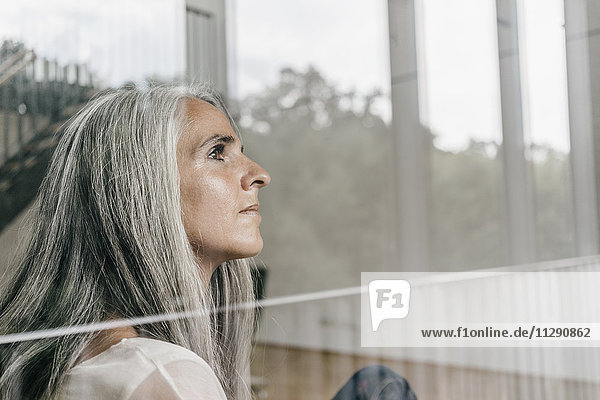 Woman with long grey hair looking out of window