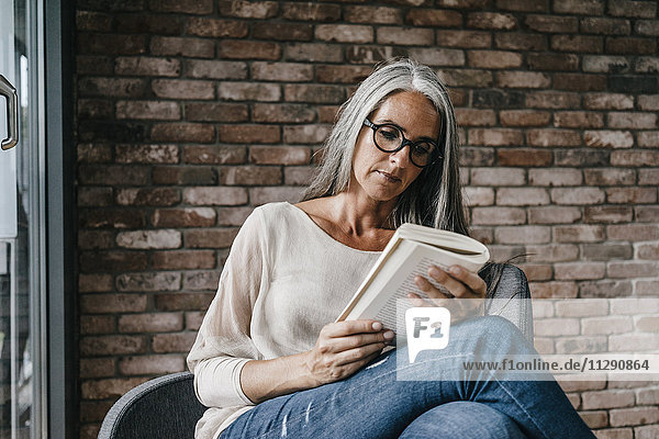 Frau mit langen grauen Haaren sitzend auf dem Stuhl Lesebuch