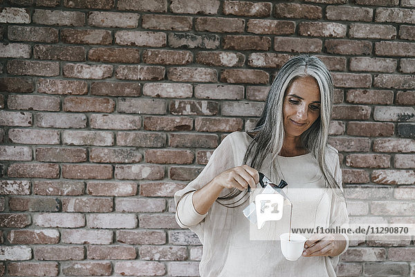 Woman with long grey hair pouring coffee into cup