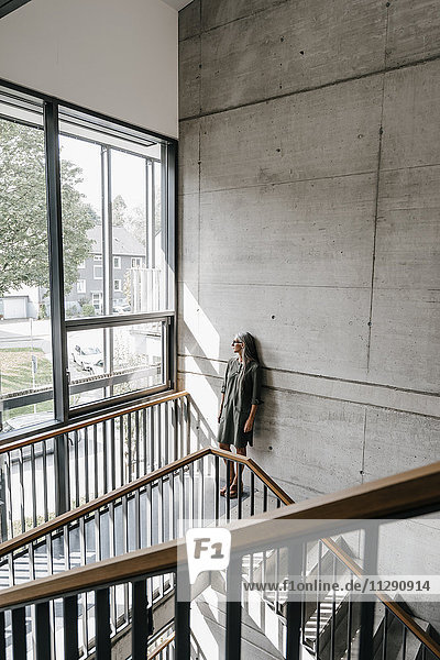 Woman with long grey hair looking out of window in staircase