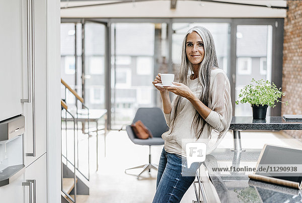 Smiling woman with long grey hair drinking coffee