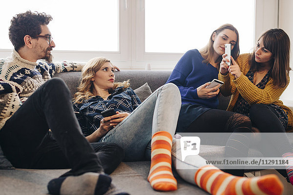 Four friends with smartphones on couch in living room hanging out