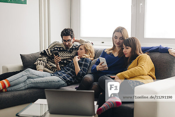 Vier Freunde mit Smartphones auf der Couch im Wohnzimmer hängen heraus