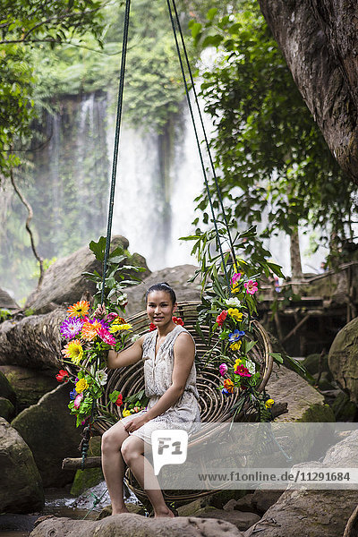 Cambodia  Nationalpark Phnom Kulen  young woman sitting on swing in front of waterfalls