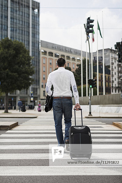 Back view of businessman with suitcase crossing the street