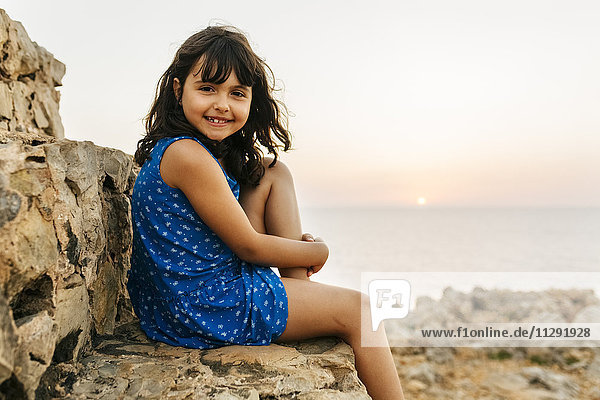 Porträt eines glücklichen kleinen Mädchens am Meer bei Sonnenuntergang