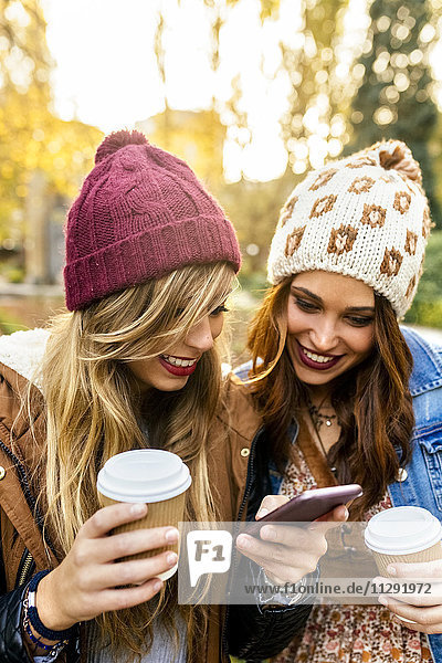 Zwei junge Frauen mit Smartphone im Herbst im Park