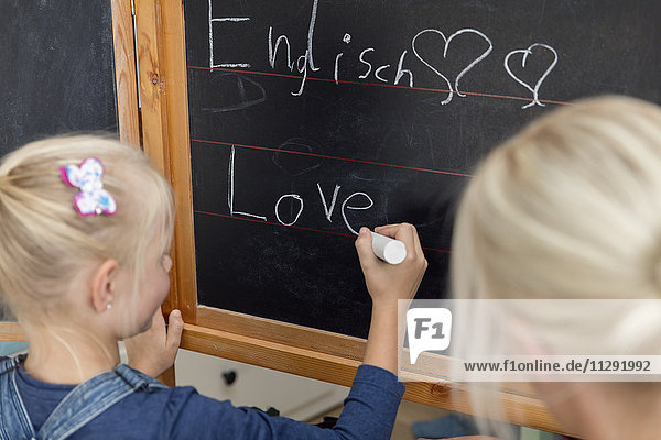 Mutter  die ihrer Tochter dabei zusieht  wie sie das Wort Liebe auf die Tafel schreibt.