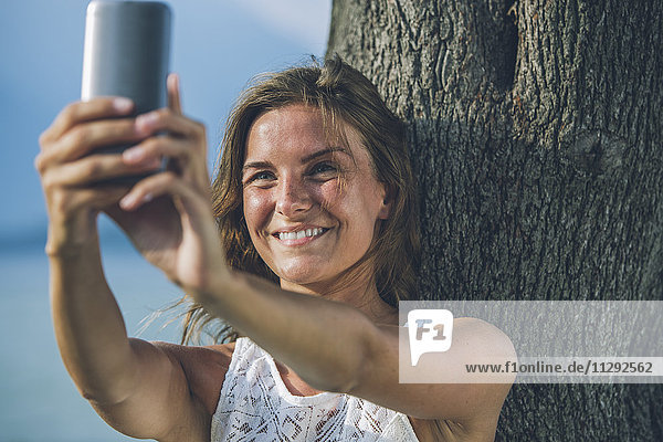 Junge Frau  die einen Selfie an einem Baum nimmt.
