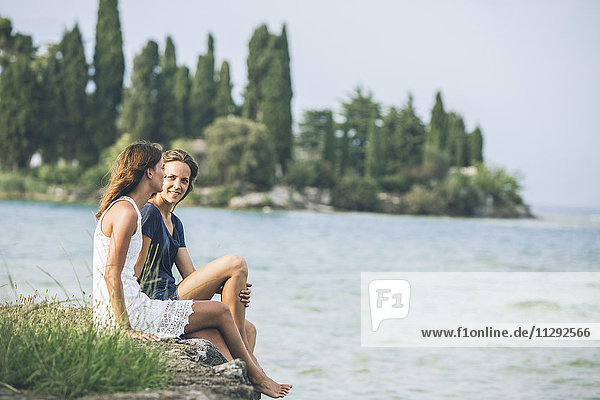 Italy  Lake Garda  two young women sitting at lakeshore