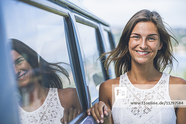 Porträt einer lächelnden jungen Frau  die sich gegen den Campingbus lehnt.