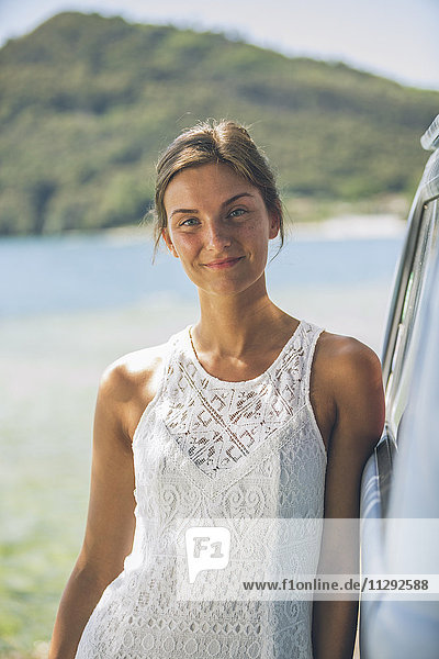 Italien  Gardasee  Porträt einer lächelnden jungen Frau  die sich gegen den Campingbus lehnt.