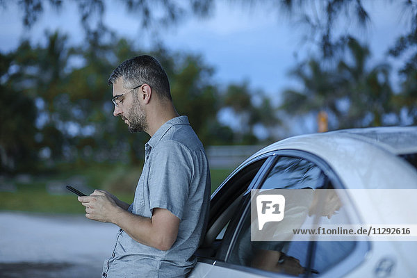 Mann mit Smartphone GPS  der sich gegen sein Auto lehnt