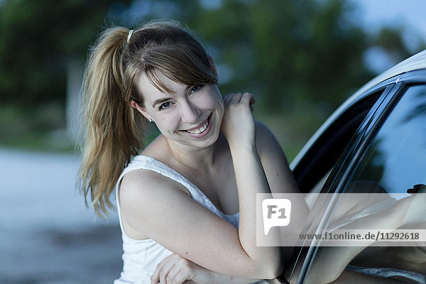 Lächelnde Frau  die sich gegen das Auto lehnt  Porträt