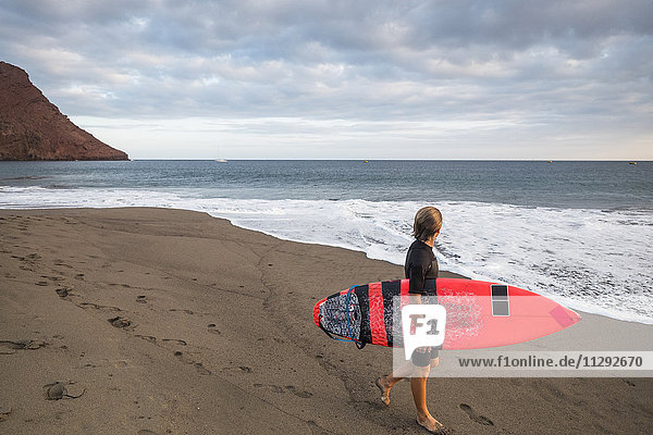 Spanien  Teneriffa  Junge mit Surfbrett am Strand