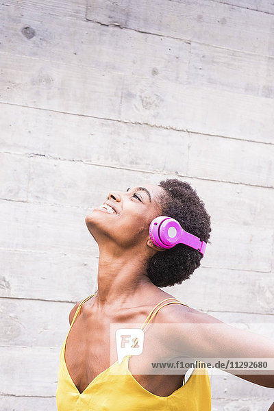 Fröhliche Frau beim Musikhören mit rosa Kopfhörern