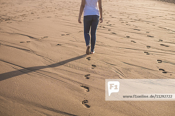 Junge Frau  die im Sand am Strand spazieren geht.