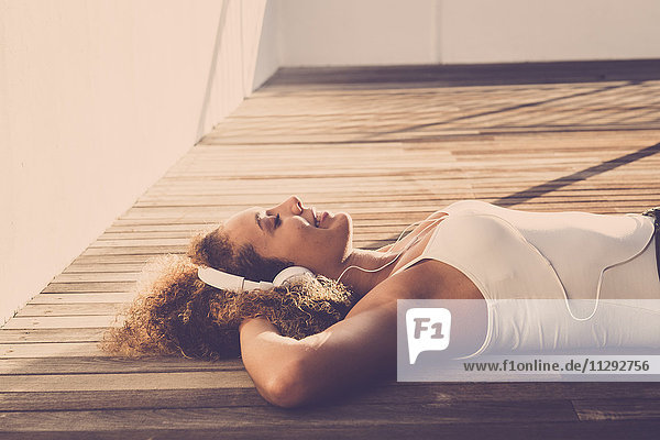 Junge Frau mit geschlossenen Augen auf Holzboden liegend Musik hören mit Kopfhörern
