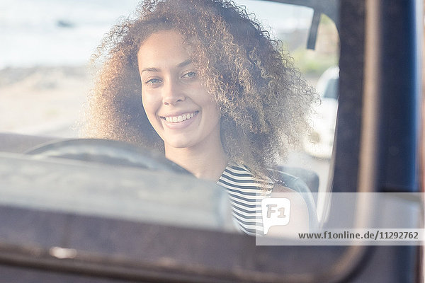 Porträt einer lächelnden jungen Frau  die hinter der Windschutzscheibe in einem Auto sitzt.