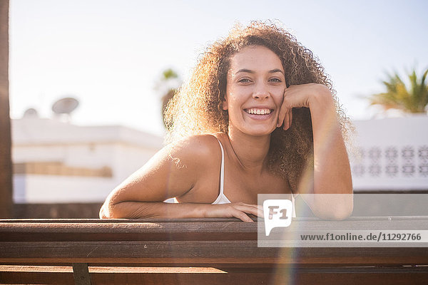 Porträt der glücklichen jungen Frau auf der Bank bei Sonnenlicht