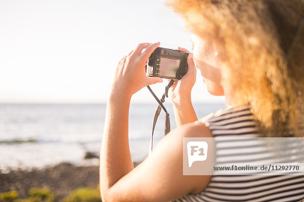 Junge Frau fotografiert das Meer mit Digitalkamera