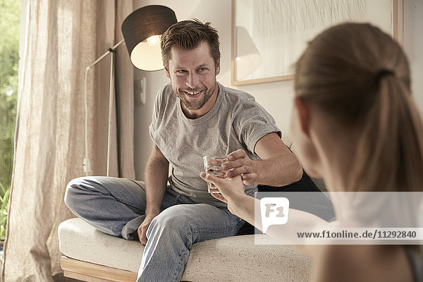 Woman handing over glass of water to man sitting on couch