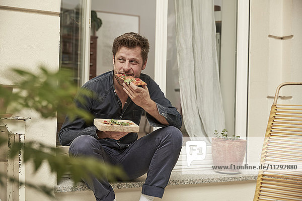 Mann isst Pizza vor der Haustür