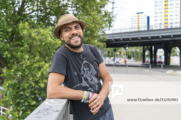 Porträt eines lächelnden Mannes mit Hut auf dem Geländer