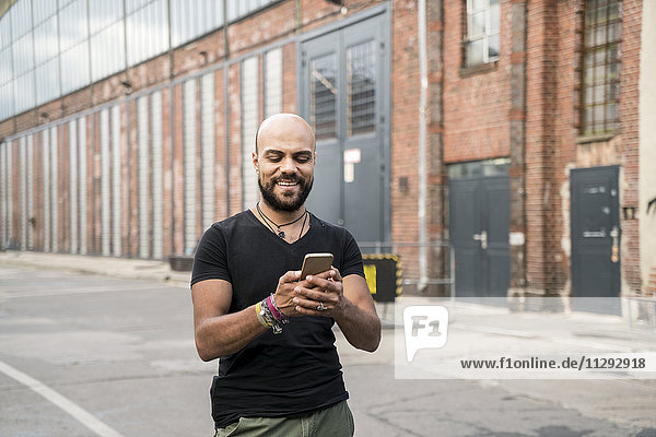 Porträt eines lächelnden Mannes  der sein Handy ansieht.